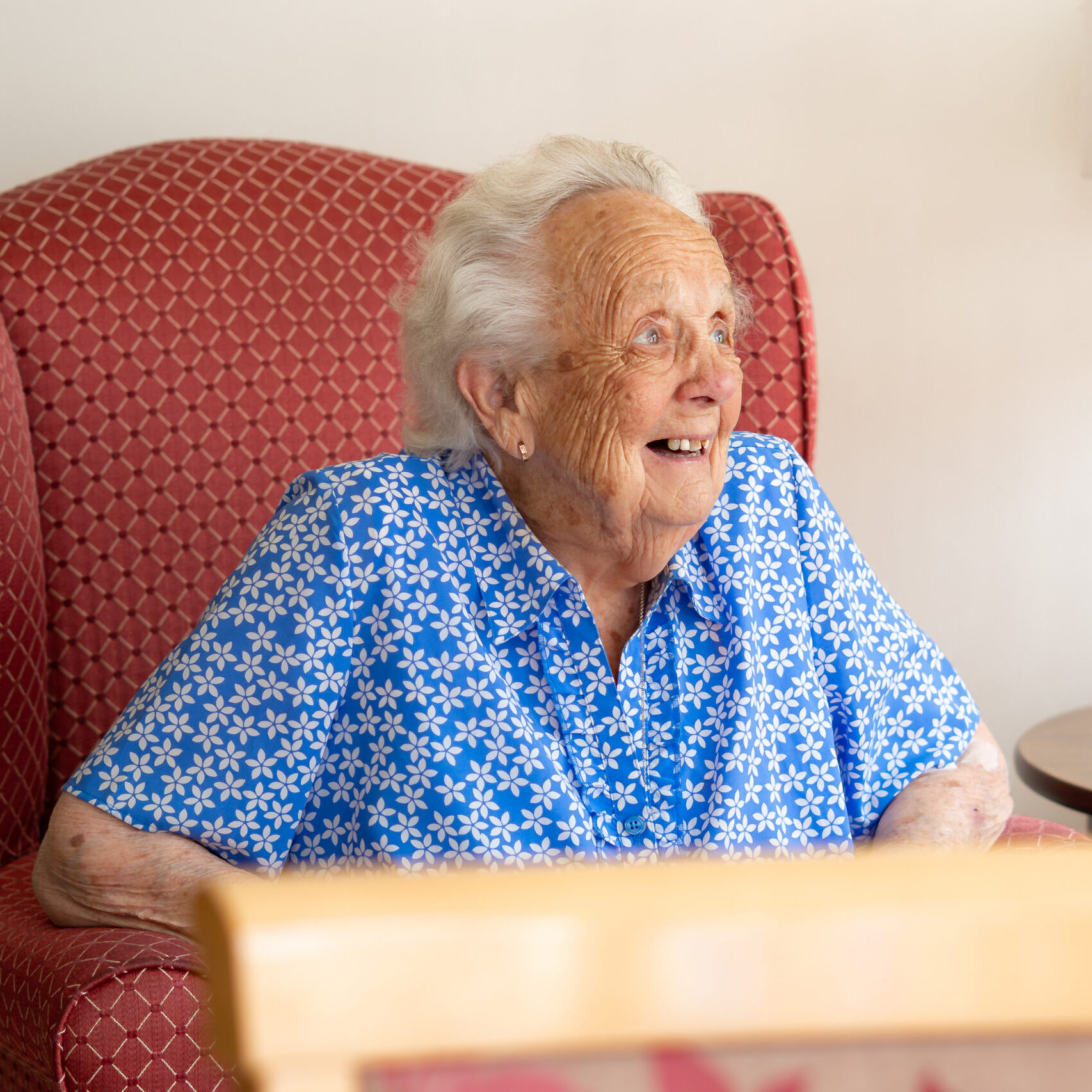 Smiling resident relaxing in an armchair at Tudor Lodge
